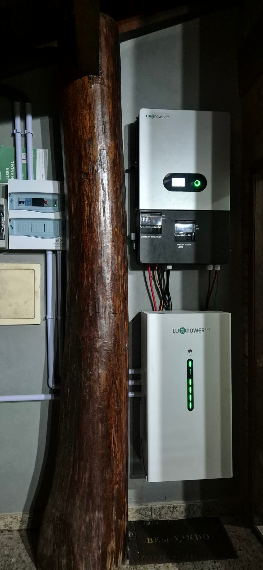 Conjunto híbrido LuxPower Tek ao lado do quadro de proteção com o adesivo da Mesaque